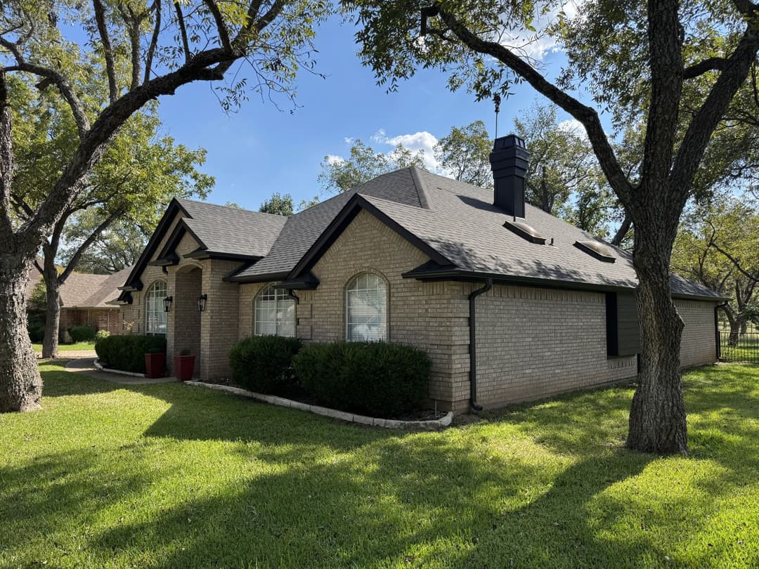 Charming single-story home with a brick exterior, lush lawn, and shaded trees.